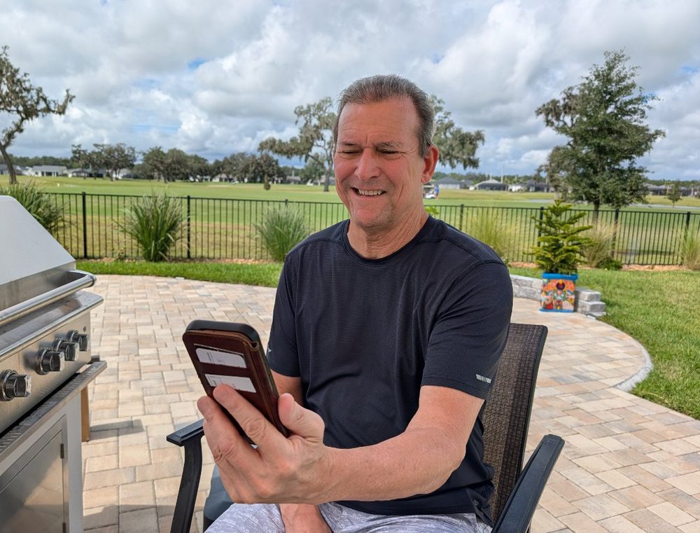 A grandfather smiling at his phone on his patio